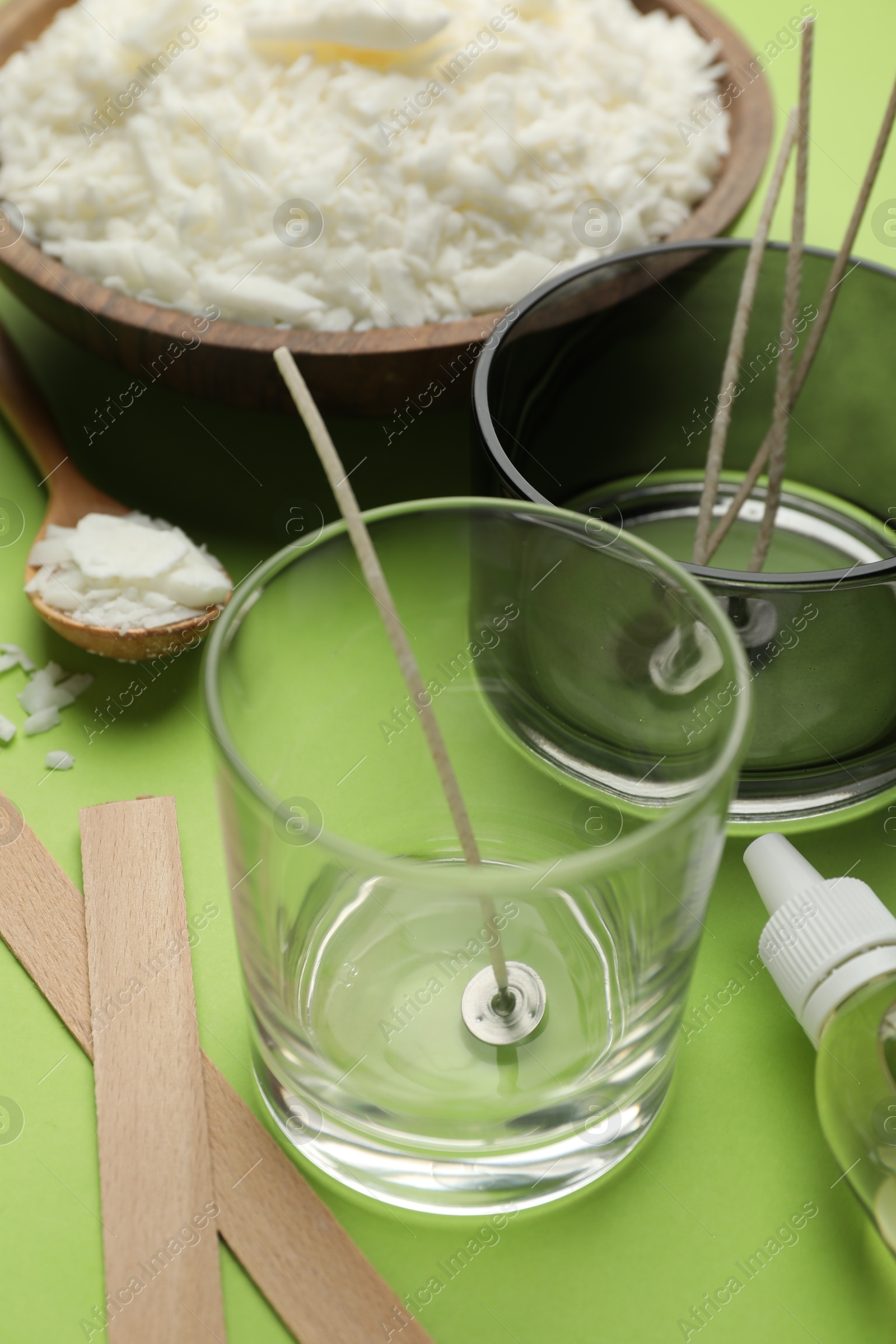 Photo of Making homemade candles. Soy wax in bowl, jars with stabilizers, wicks and essential oil on green background, closeup