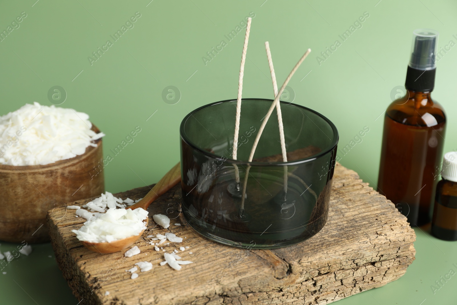 Photo of Soy wax, essential oils, different tools for making candles and piece of wood on green background, closeup