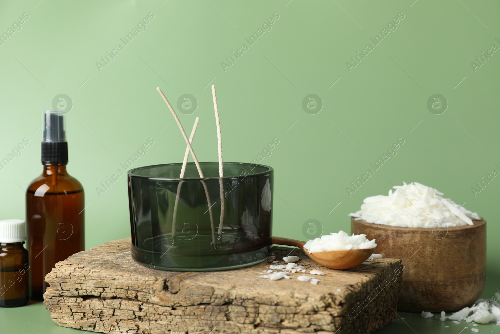 Photo of Soy wax, essential oils, different tools for making candles and piece of wood on green background