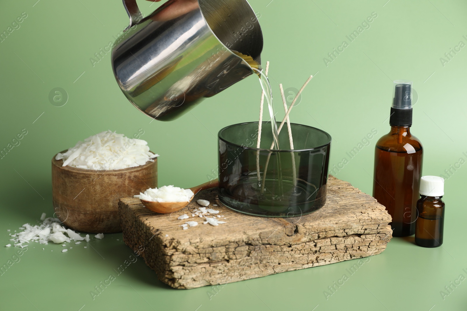 Photo of Making handmade candles. Pouring melted soy wax into jar on green background, closeup