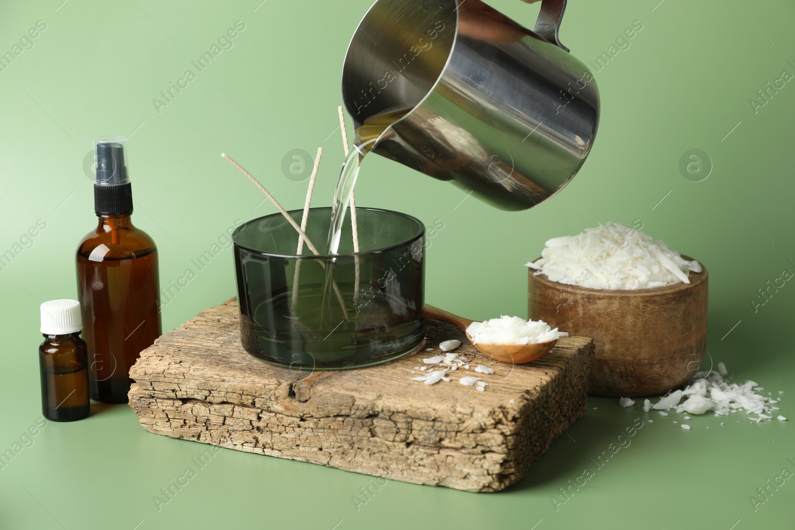 Photo of Making handmade candles. Pouring melted soy wax into jar on green background, closeup