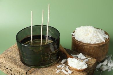 Photo of Making homemade candles. Soy wax, jar with wicks and spoon on green background, closeup