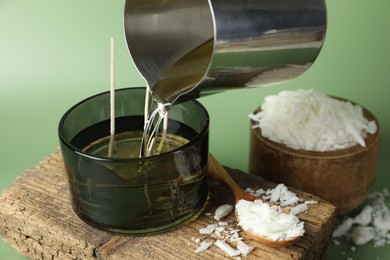 Photo of Making handmade candles. Pouring melted soy wax into jar on green background, closeup