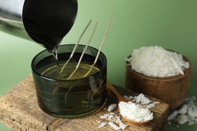 Photo of Making handmade candles. Pouring melted soy wax into jar on green background, closeup