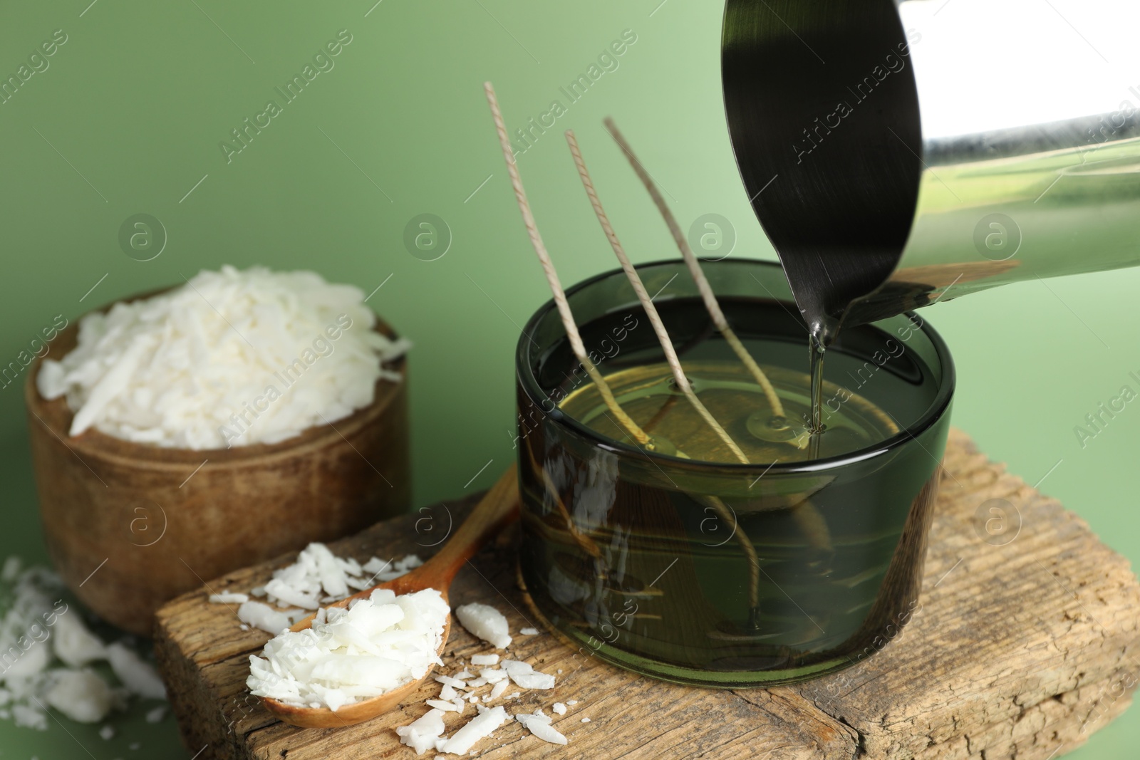 Photo of Making handmade candles. Pouring melted soy wax into jar on green background, closeup