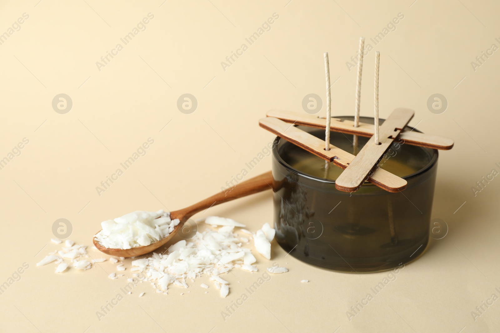 Photo of Soy wax candle with wicks, stabilizers and spoon on beige background, space for text