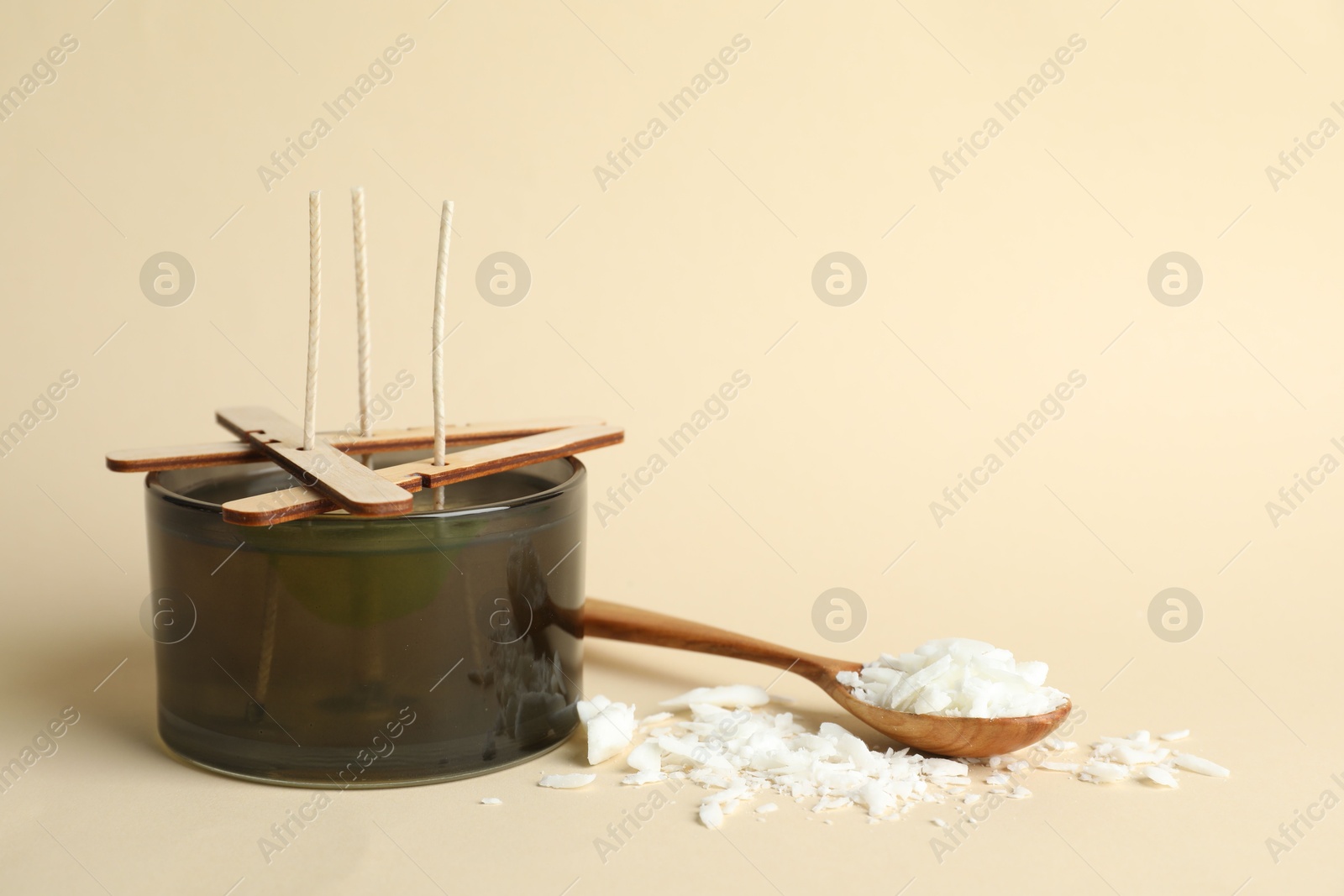 Photo of Soy wax candle with wicks, stabilizers and spoon on beige background, space for text