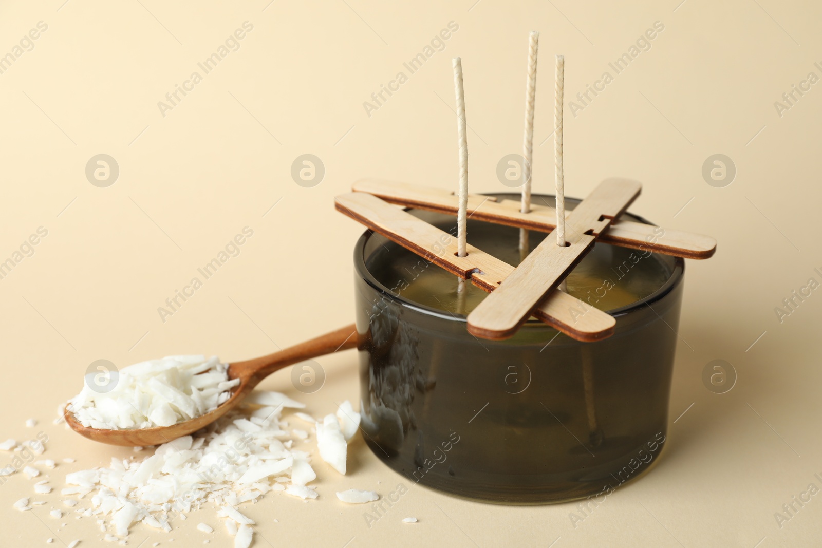 Photo of Soy wax candle with stabilizers and spoon on beige background