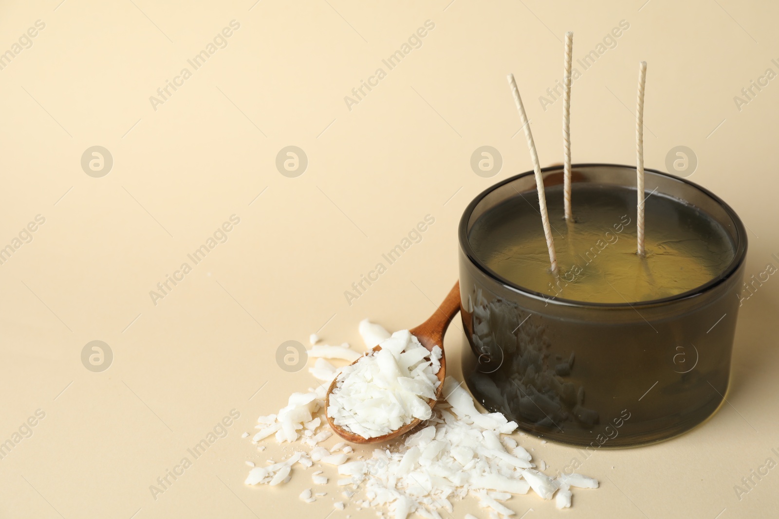 Photo of Soy wax, candle and spoon on beige background, closeup. Space for text