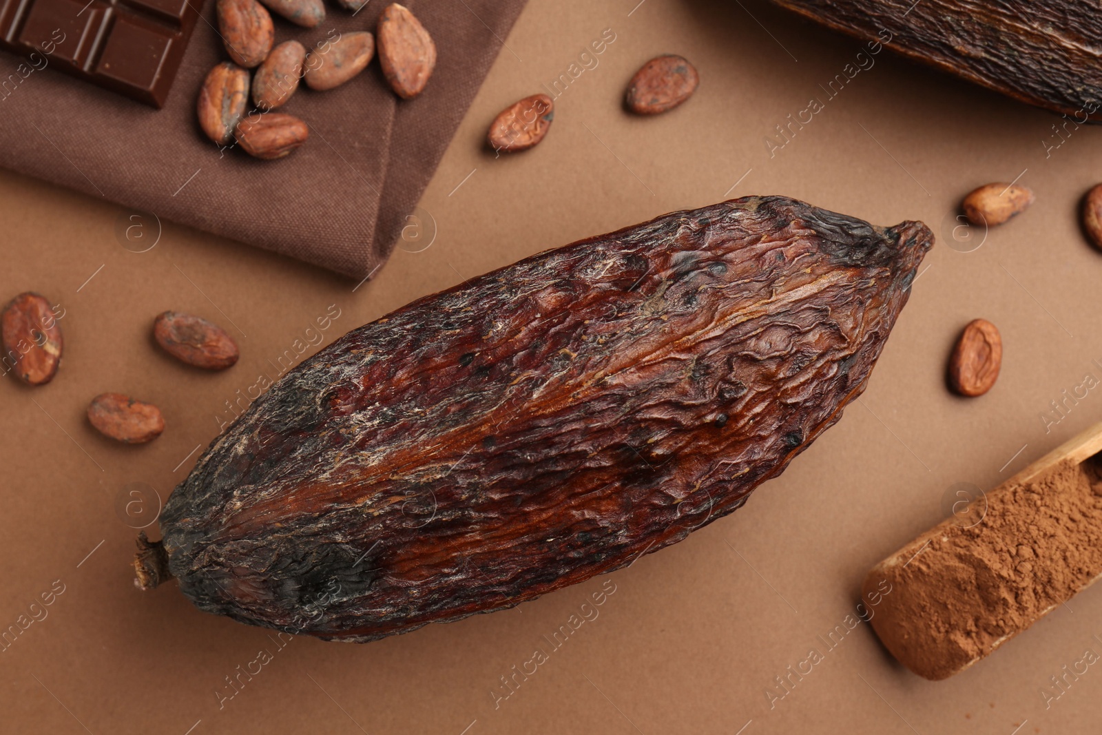 Photo of Cocoa pod, scoop with powder and beans on brown background, flat lay