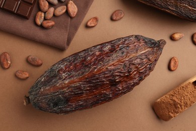 Cocoa pod, scoop with powder and beans on brown background, flat lay