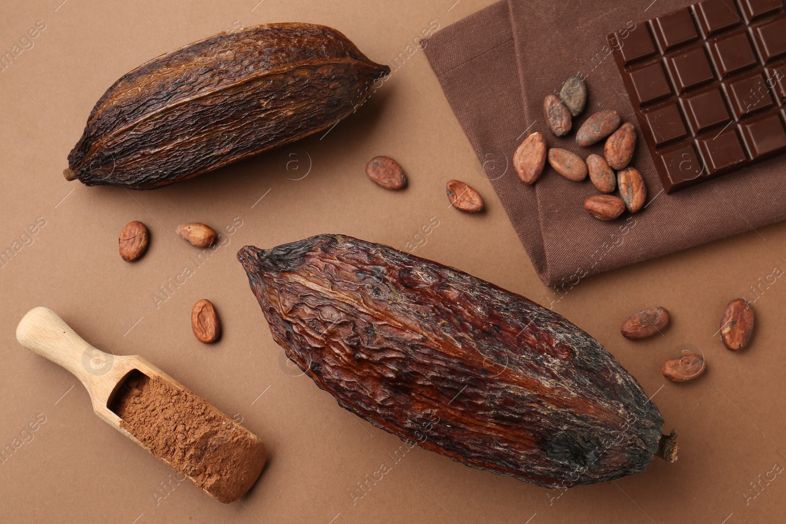 Photo of Cocoa pods, scoop with powder, beans and chocolate bar on brown background, flat lay