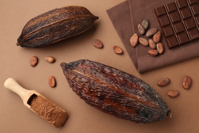 Cocoa pods, scoop with powder, beans and chocolate bar on brown background, flat lay