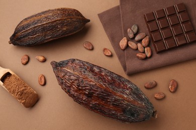 Cocoa pods, scoop with powder, beans and chocolate bar on brown background, flat lay