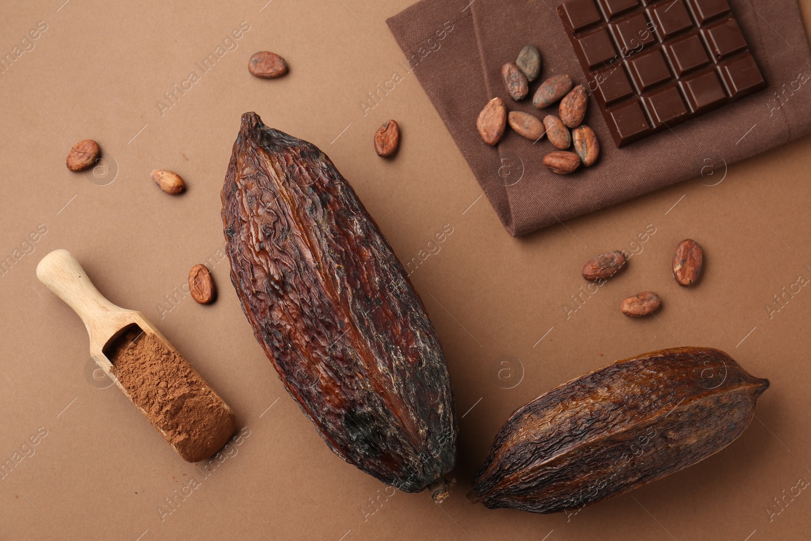 Cocoa pods, scoop with powder, beans and chocolate bar on brown background, flat lay Photo of Cocoa pods, scoop with powder, beans and chocolate bar on brown background, flat lay