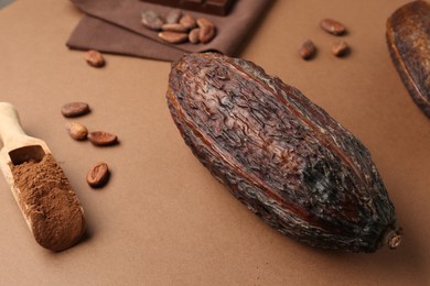 Photo of Cocoa pod, scoop with powder and beans on brown background, closeup