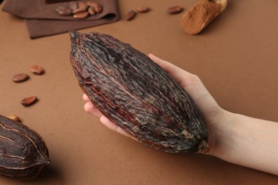 Woman with cocoa pod on brown background, closeup