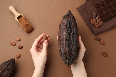 Woman with cocoa pod on brown background, top view