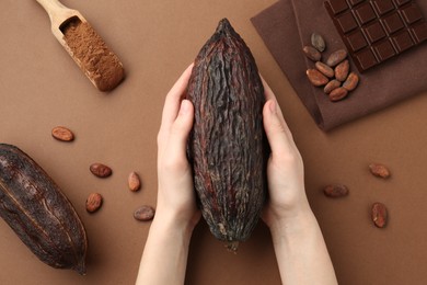 Photo of Woman with cocoa pod on brown background, top view