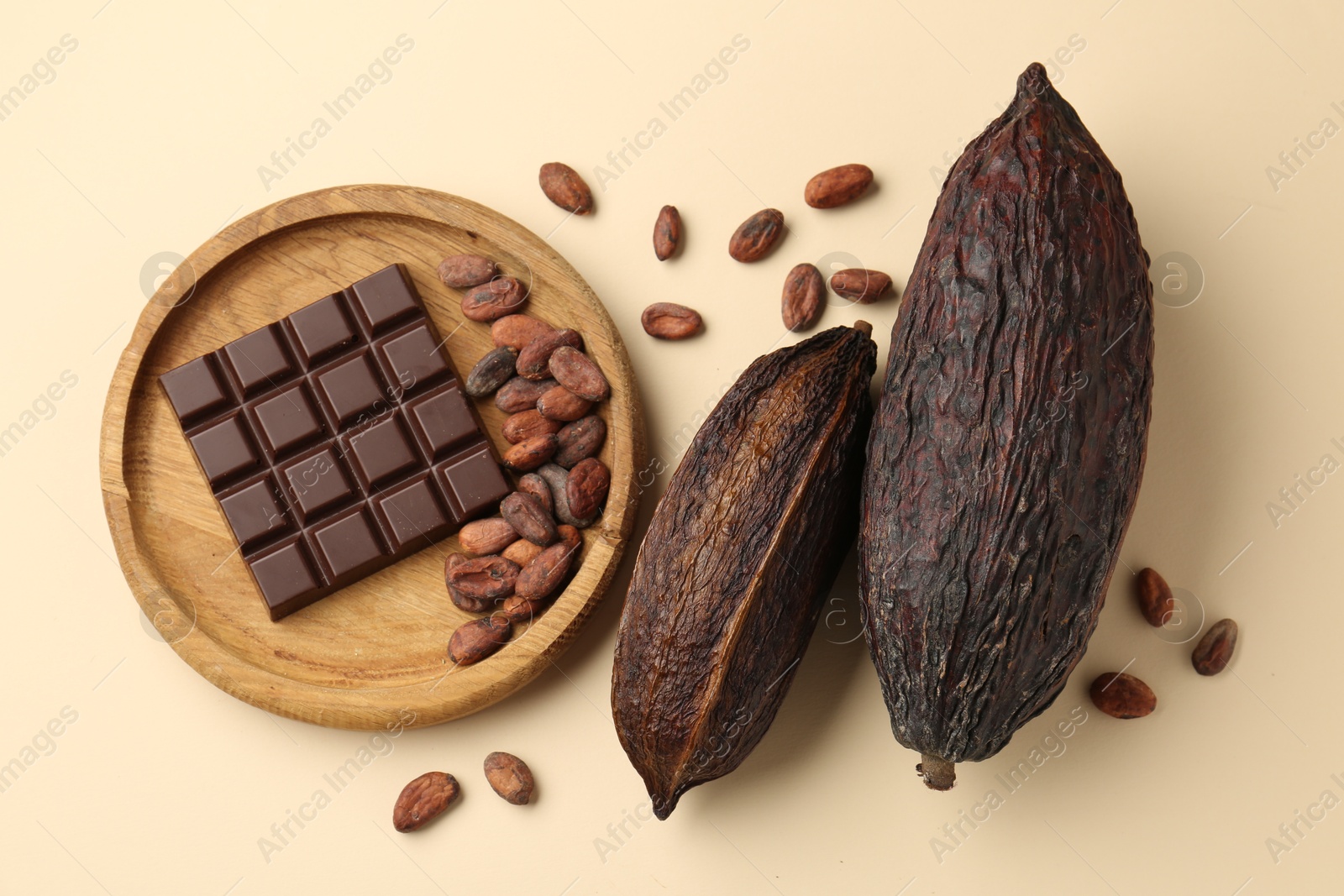 Photo of Cocoa pods, beans and chocolate bar on beige background, flat lay