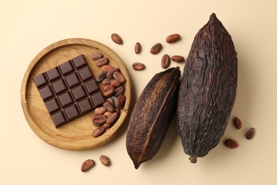 Cocoa pods, beans and chocolate bar on beige background, flat lay