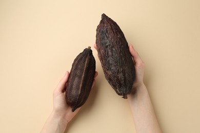 Woman with cocoa pods on beige background, top view