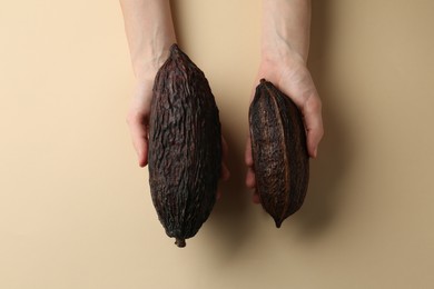 Woman with cocoa pods on beige background, top view