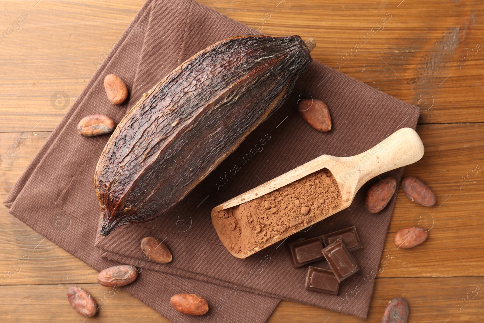 Photo of Cocoa pod, scoop with powder, beans and chocolate pieces on wooden table, flat lay