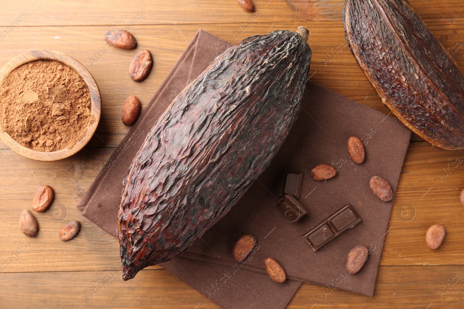 Photo of Cocoa pods, powder in bowl, beans and chocolate pieces on wooden table, flat lay