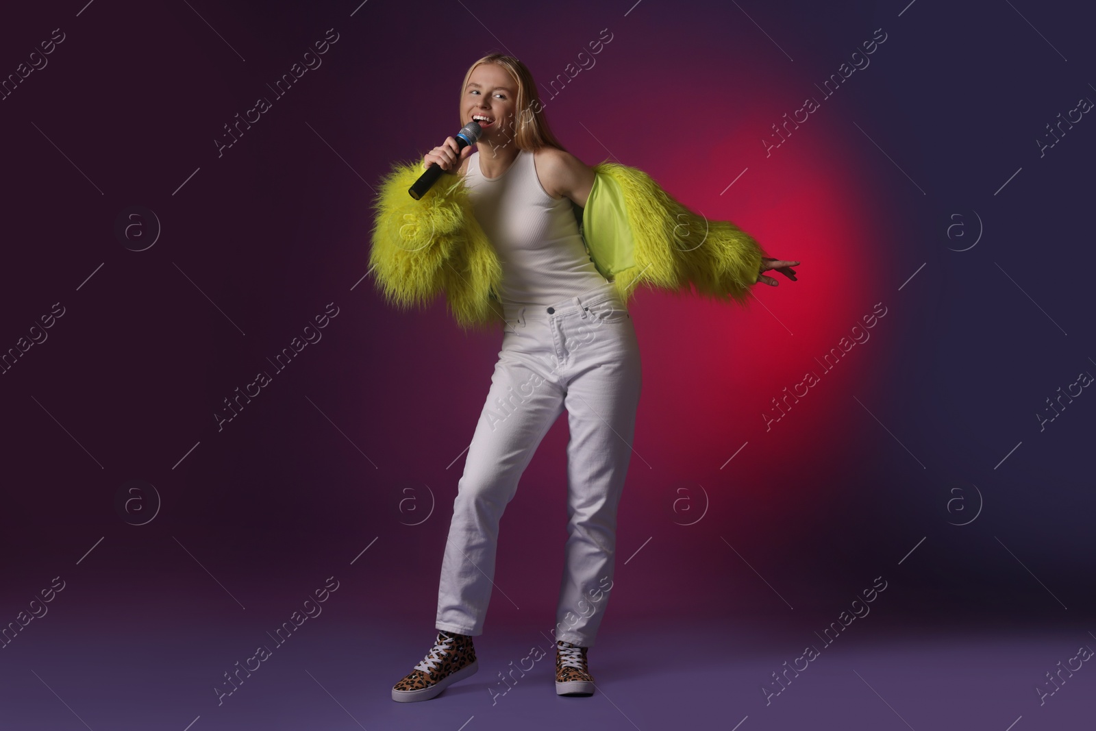 Photo of Talented singer in faux fur performing on dark background with pink light