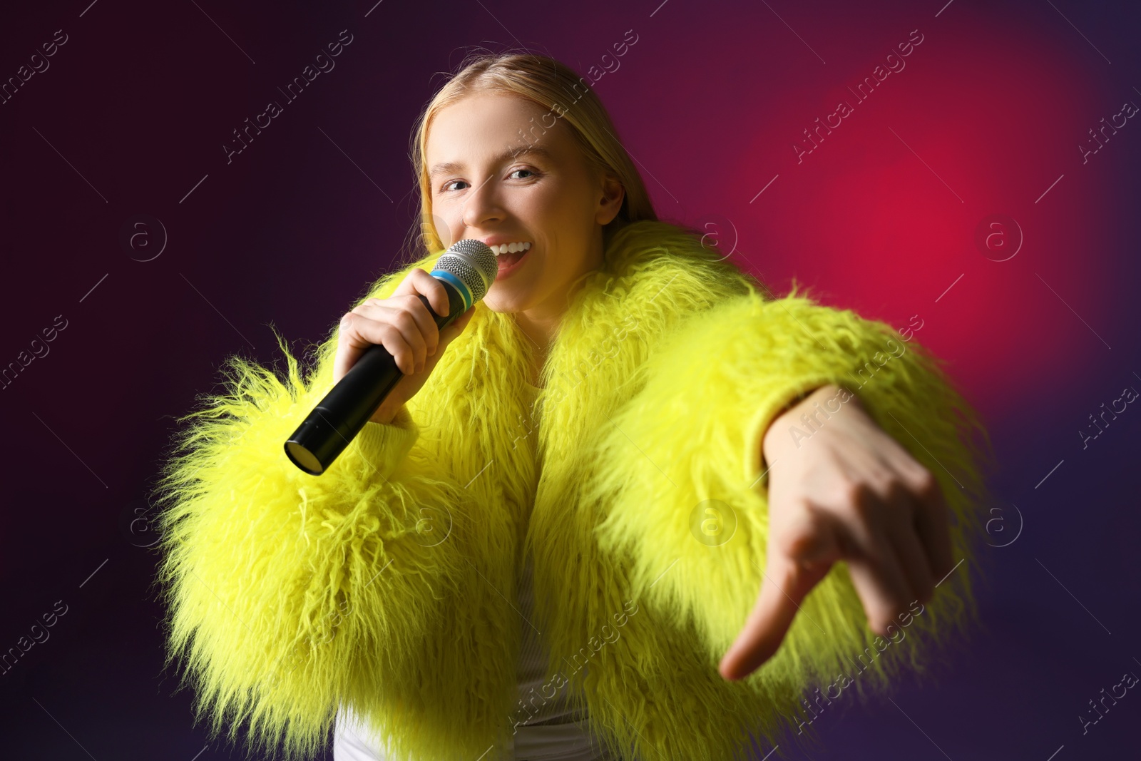 Photo of Talented singer in faux fur performing on dark background with pink light