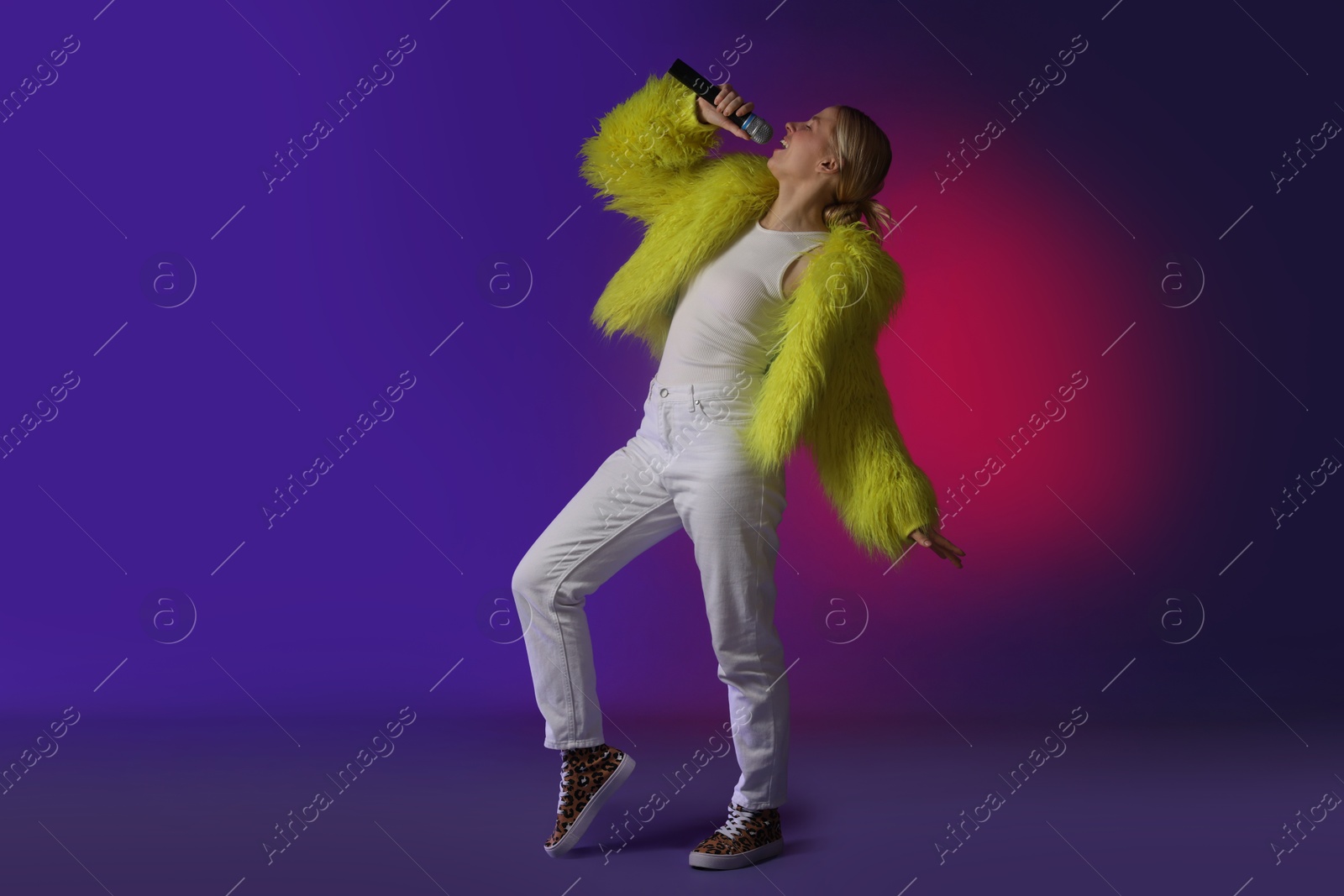 Photo of Talented singer in faux fur performing on purple background with pink light