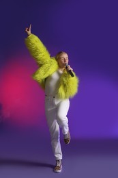 Photo of Talented singer in faux fur performing on purple background with pink light