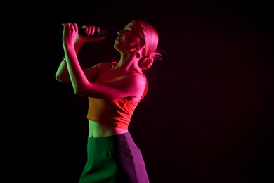 Photo of Beautiful singer performing on dark background in color lights. Space for text