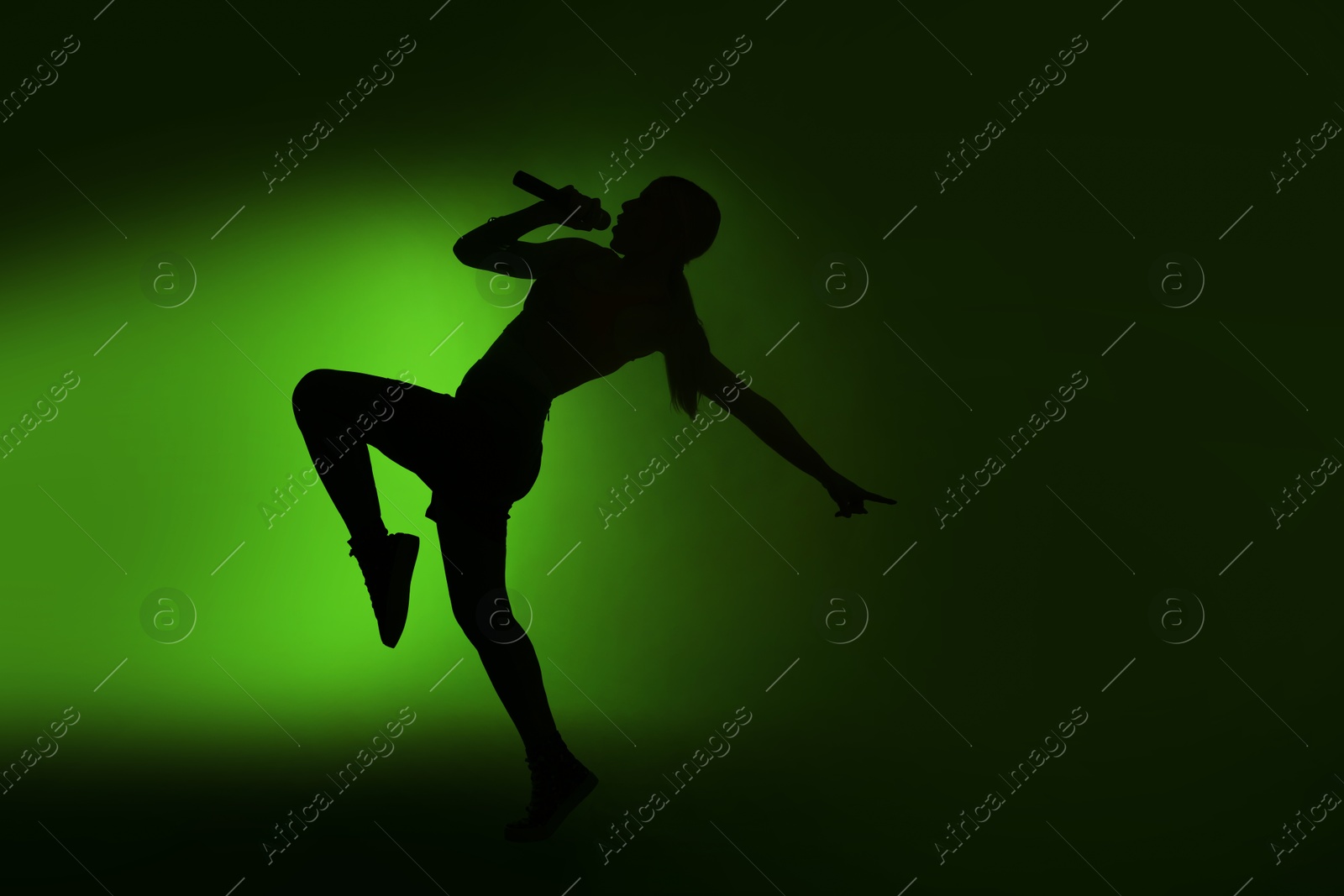 Photo of Silhouette of woman singing on dark background with green light