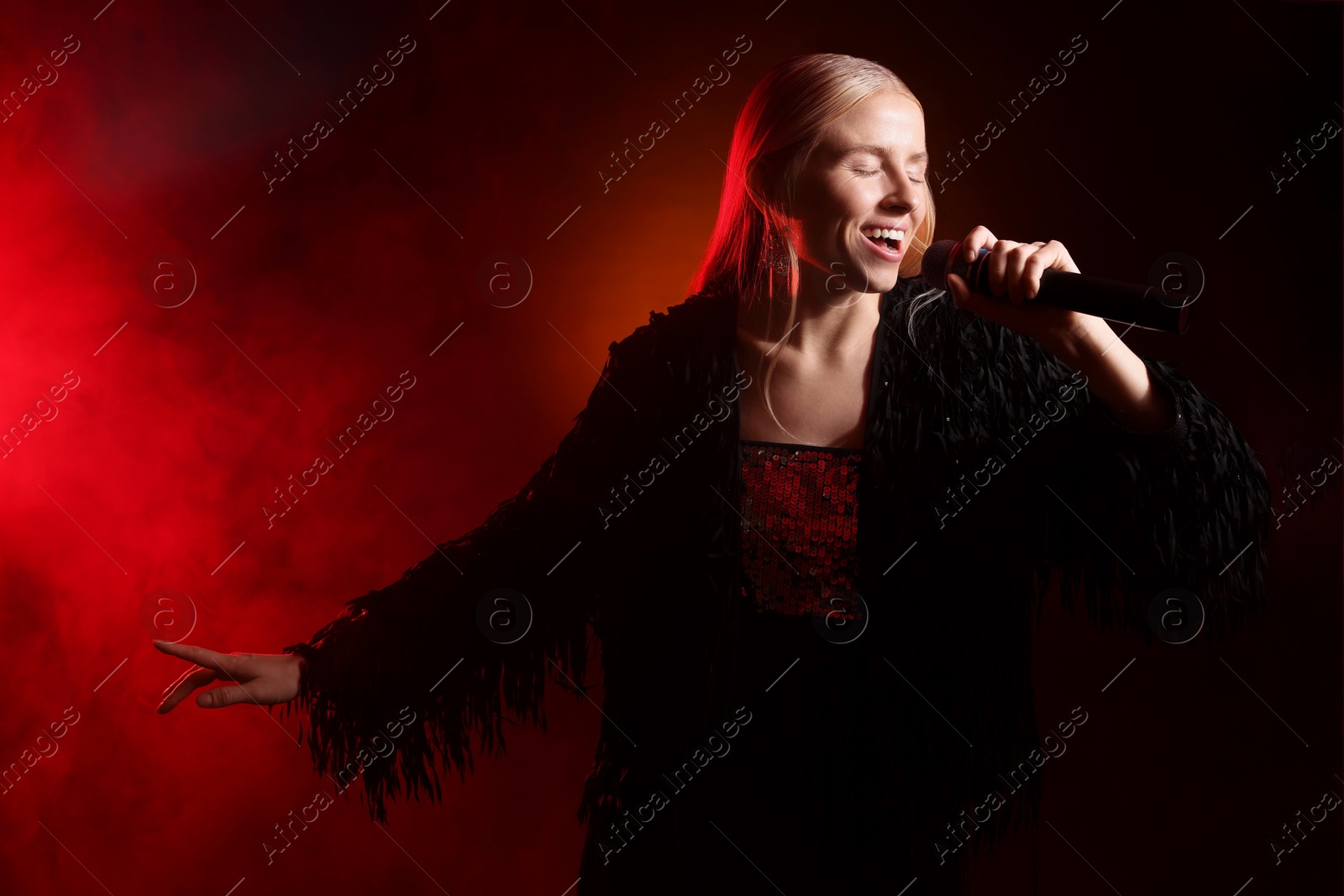 Photo of Beautiful singer performing on dark background with red light and smoke. Space for text