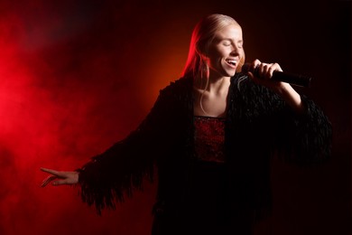 Photo of Beautiful singer performing on dark background with red light and smoke. Space for text