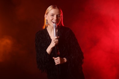 Photo of Beautiful singer performing on dark background with red light and smoke