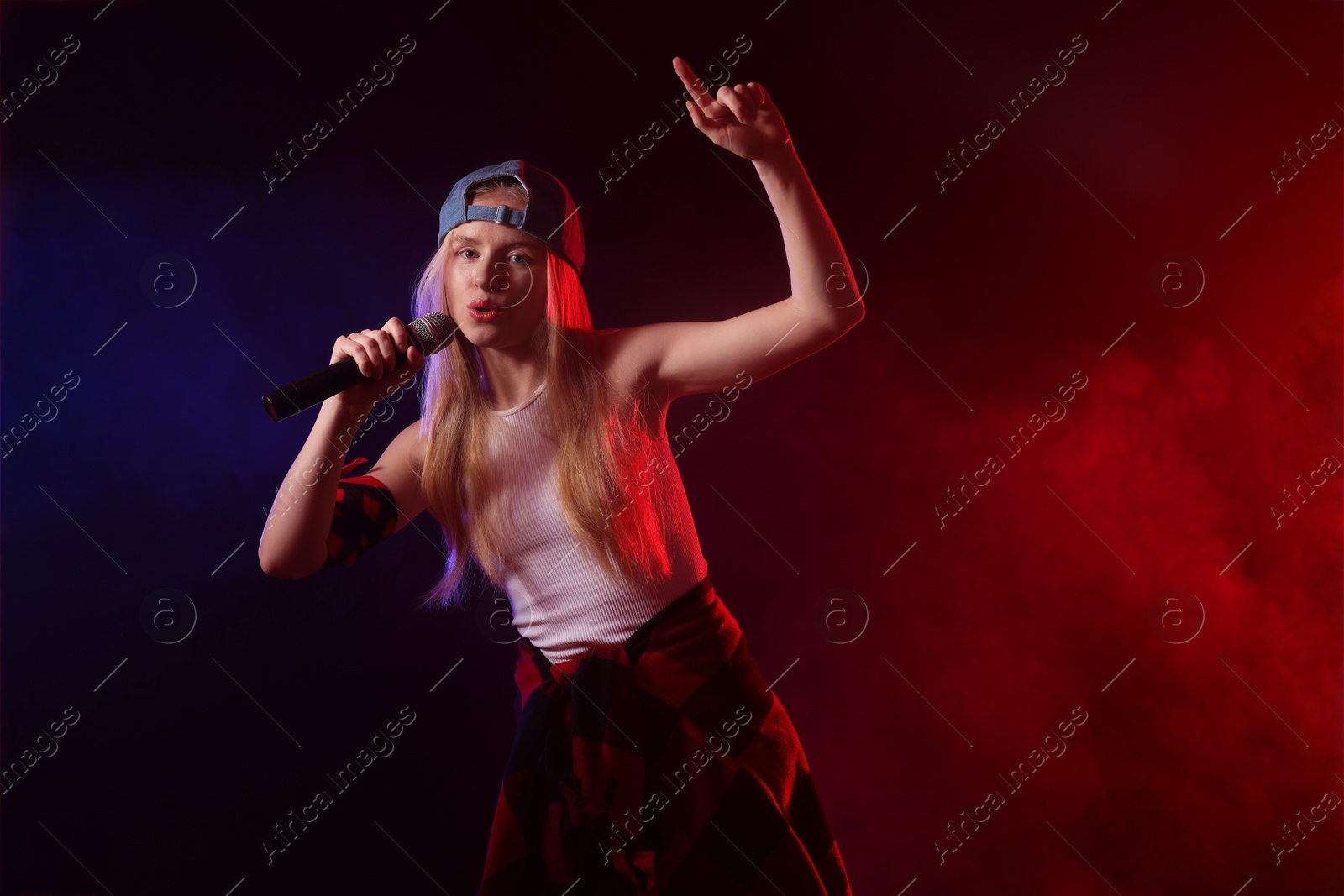 Photo of Talented singer performing on dark background with color lights and smoke