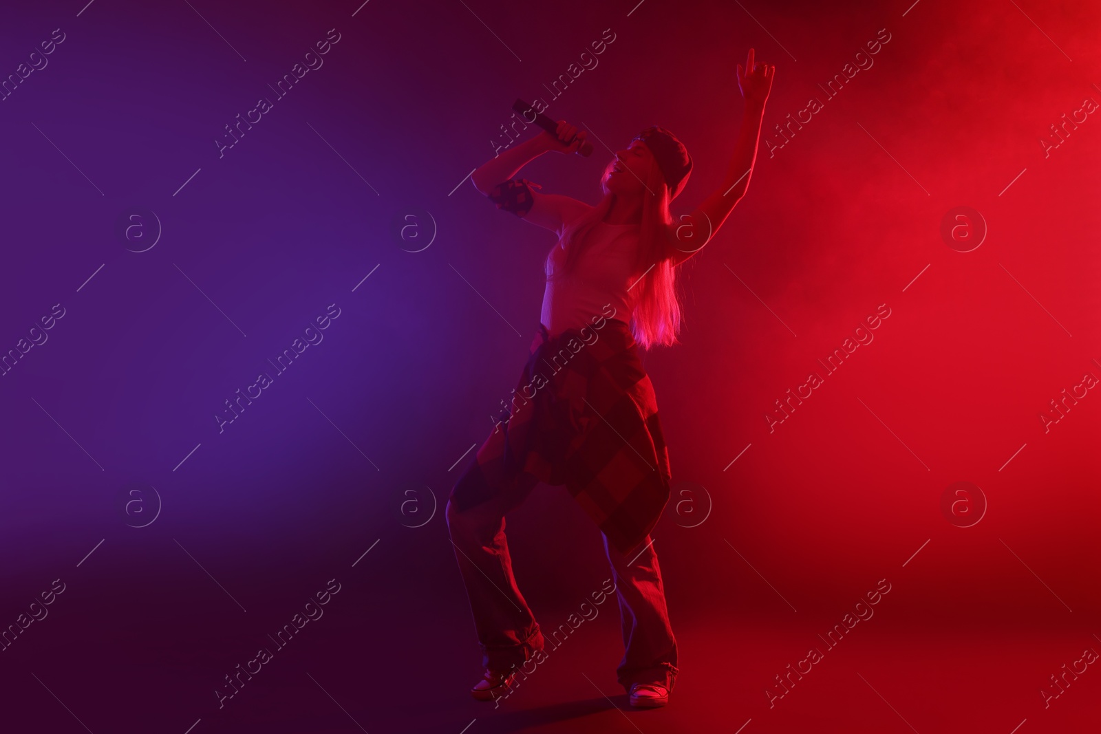 Photo of Talented singer performing on dark background with color lights and smoke