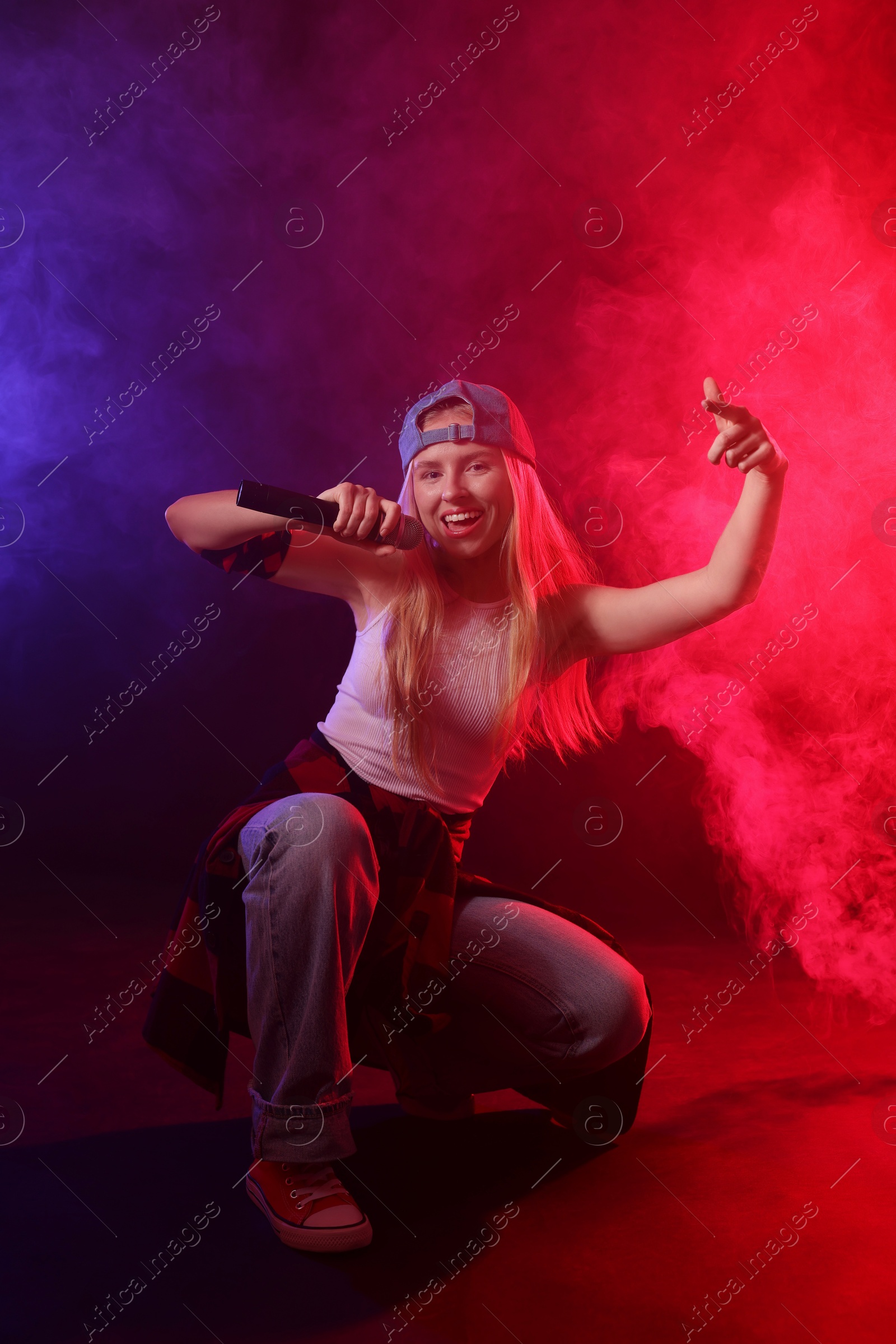 Photo of Talented singer performing on dark background with color lights and smoke