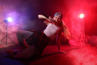 Photo of Talented singer performing on dark background with color lights and smoke