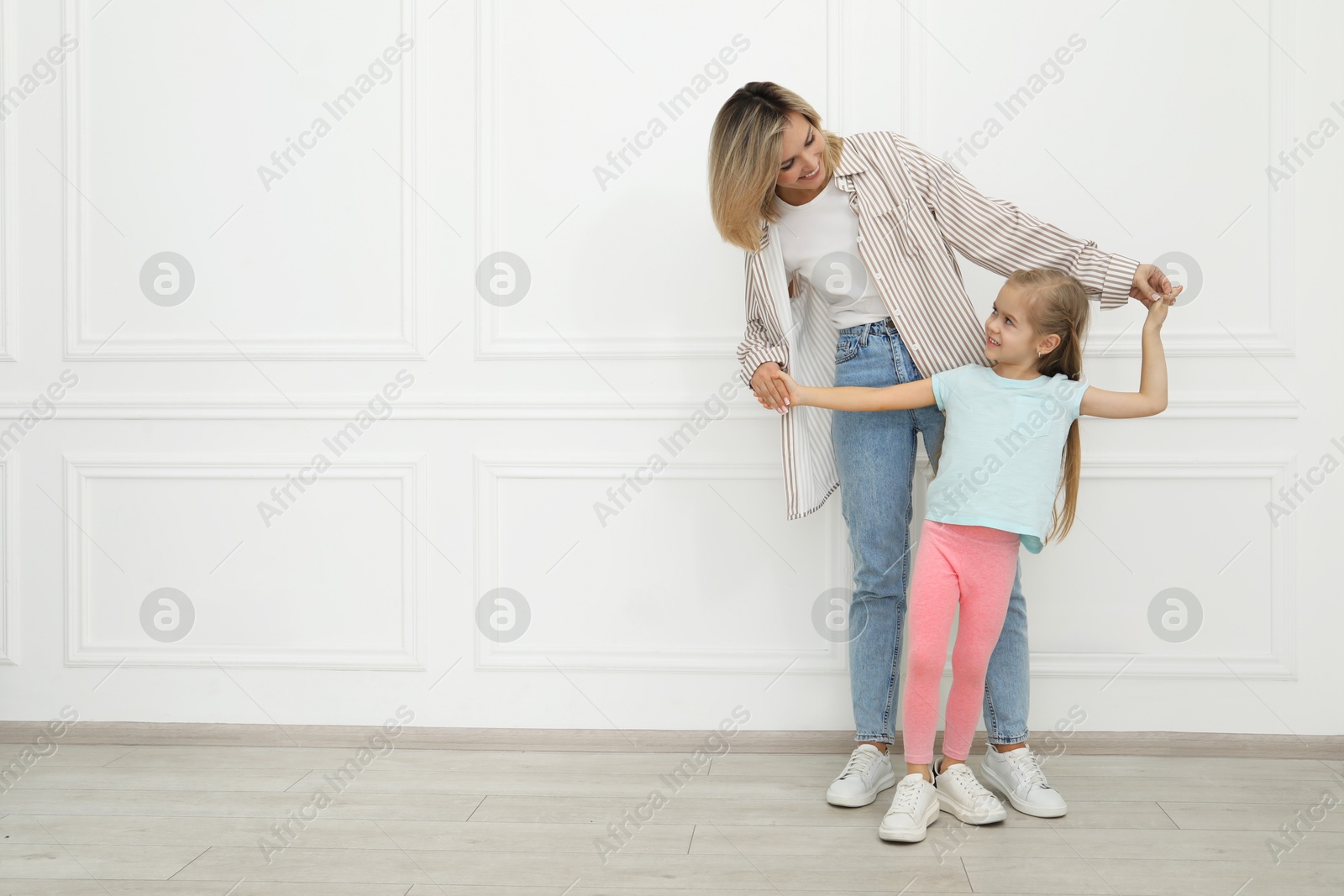 Photo of Happy mother and her cute little daughter near white wall indoors