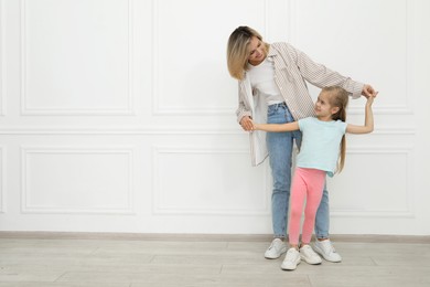 Photo of Happy mother and her cute little daughter near white wall indoors