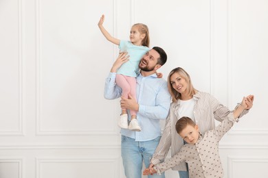 Happy parents and their children near white wall indoors, space for text