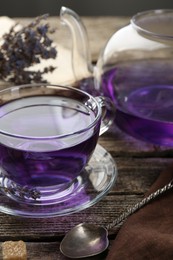 Aromatic lavender tea in glass cup, spoon, teapot and dry flowers on wooden table, closeup