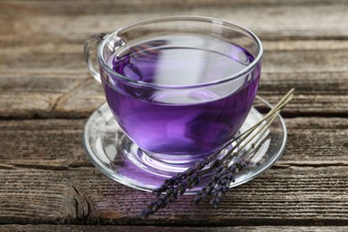 Photo of Aromatic lavender tea in glass cup and dry flowers on wooden table, closeup