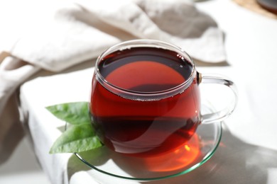 Photo of Refreshing black tea in cup on light table, closeup