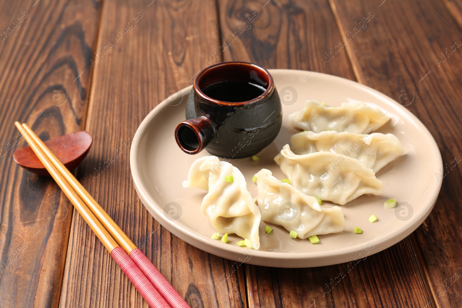 Photo of Tasty gyoza (dumpling), soy sauce and chopsticks on wooden table, closeup