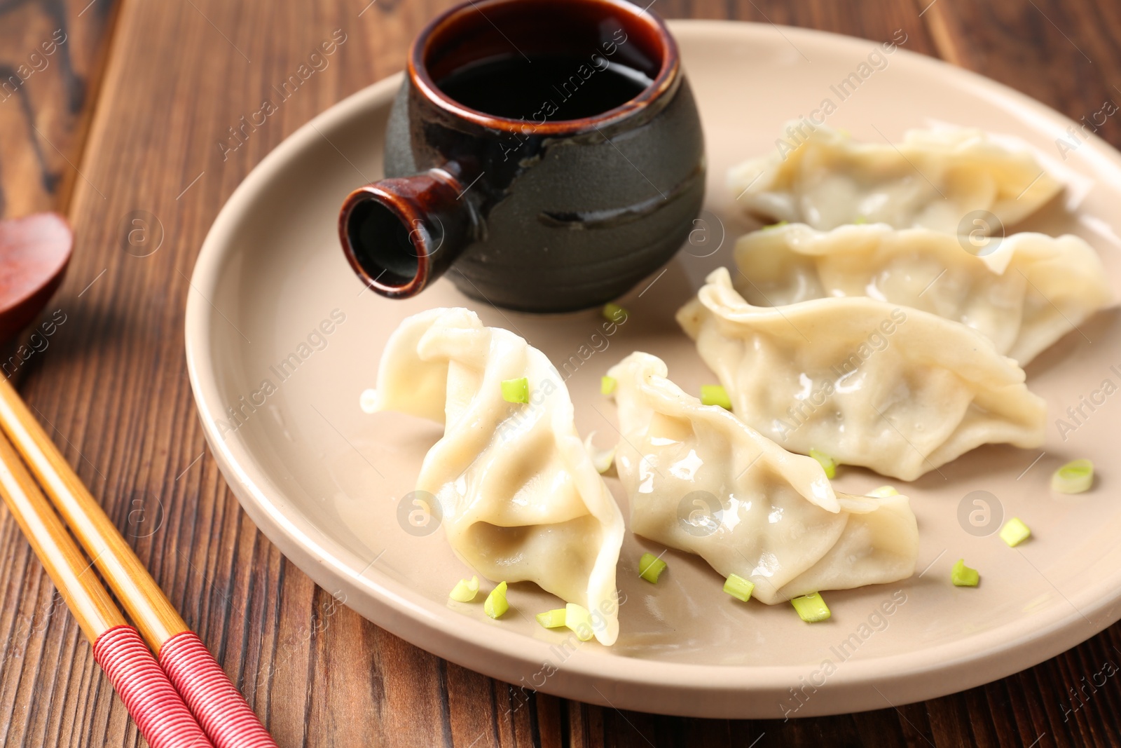 Photo of Tasty gyoza (dumpling), soy sauce and chopsticks on wooden table, closeup